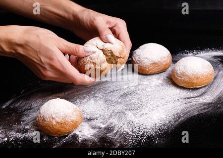 Homemade pastries. White buns are separated by hand. Photo of baking on a black background. Donuts sprinkled with powder. Stock Photo