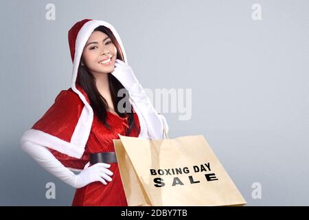 Asian woman in Santa costume holding shopping bag with Boxing Day Sale text with white background Stock Photo