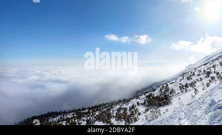 View from the snow covered mountain in winter to temperature inversion forming sea of clouds seen from above. Stock Photo