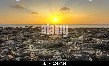 Rocky beach uncovered in low tide during evening sunset light with some clouds over horizon. Koh Lanta, Thailand Stock Photo