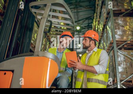 Two warehouse workers in helmets having a conversation Stock Photo
