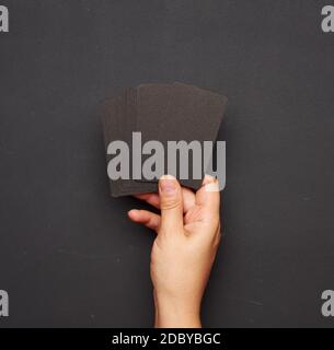 female hand holding a stack of blank black business cards against a background of empty black chalk board Stock Photo