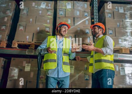 Two workers in yellow vests discussing something in the warehouse Stock Photo