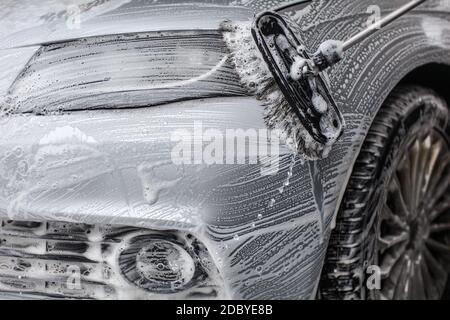 Detail on car front covered in soap foam,  washed with brush in carwash. Stock Photo