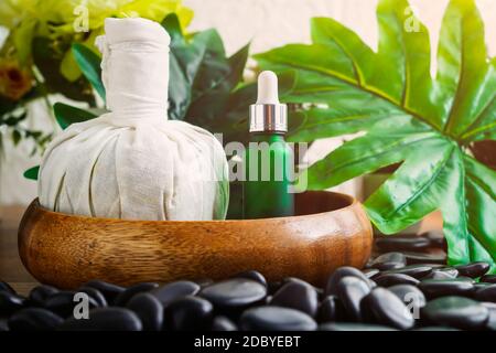 Thai Spa massage setting with serum oil bottle dropper mock up or essential oil and thai herbal compress balls on black stone against green leave back Stock Photo