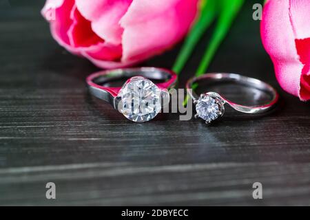 Close up Diamond gem wedding rings with pink tulip flower on black background Stock Photo