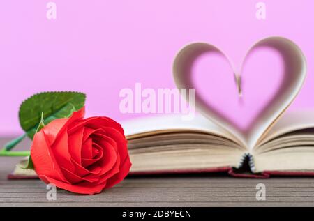 Pages of book curved into a heart shape and red rose. Love concept of heart shape from book pages on pink background Stock Photo