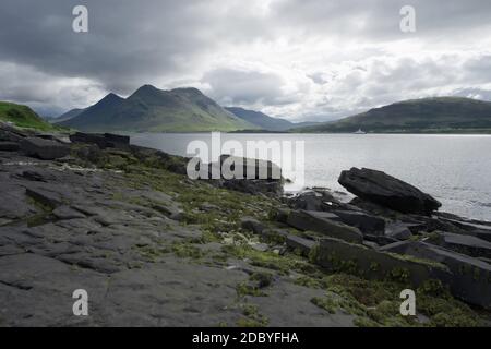 Coastal landscape from the isle of raasay looking towards the isle of skye. Ferry travels the sea under the peak of Glamaig which is cloud topped. Stock Photo