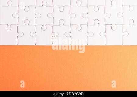 Top view flat lay of paper plain white jigsaw puzzle game texture on an orange background, quiz calculation concept Stock Photo