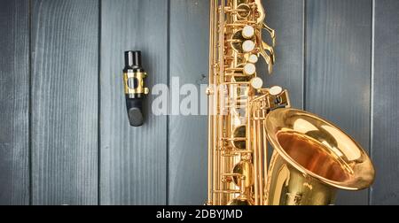 Saxophone mouthpiece disassembled from the body of the instrument, with dental guard and gold clamp, on gray wood Stock Photo