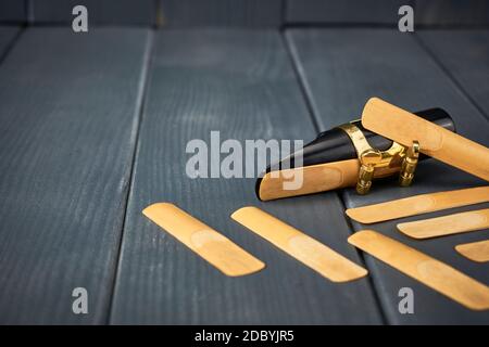saxophone mouthpiece and reed with clamp and gold hardware along with replacement reeds on gray wooden background Stock Photo