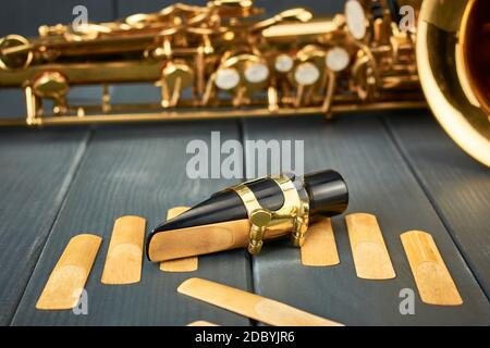 saxophone mouthpiece and reed with clamp and gold hardware along with spare reeds on gray wooden background and sax body Stock Photo