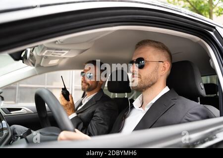 Security Guard In Sunglasses Inside Car Talking On Walkie Talkie Stock Photo