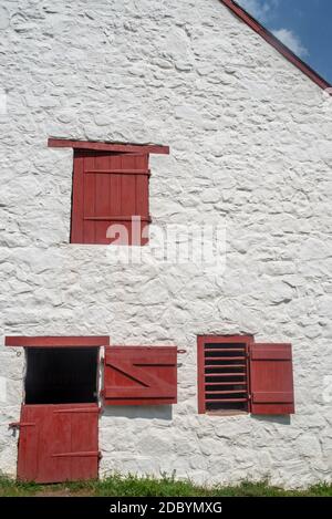 Full frame in natural light with copy space. Image shows red door, shutters, and slatted window on a whitewashed stone wall. Stock Photo