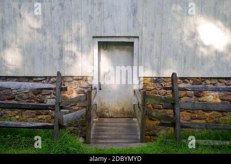Recessed door sits back  from green grass and wooden fence, centered in dappled golden hour sunlight. Stock Photo