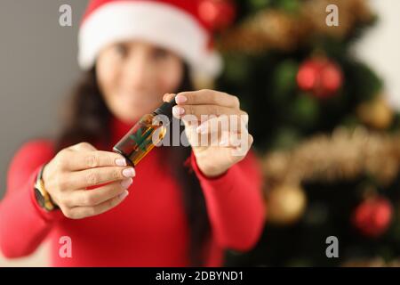 Woman in santa claus hat holding a bottle with marijuana extract near the christmas tree Stock Photo
