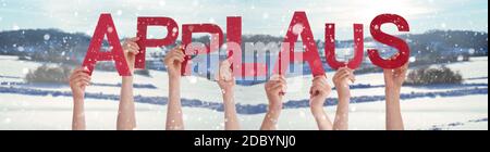 People Hands Holding Colorful German Word Applaus Means Applause. Snowy Winter Background With Snowflakes Stock Photo