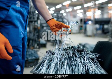 Worker in uniform shows new bicycle spokes on factory. Bike wheels assembly in workshop, cycle parts installation Stock Photo