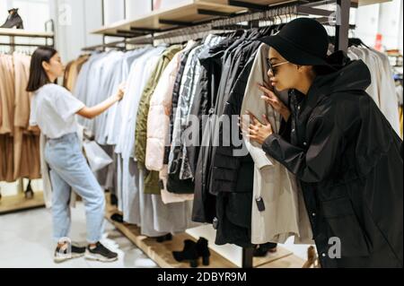 Two cute girls buying clothes in clothing store. Women shopping in