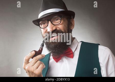 The smiling elegant bearded man is smoking tobacco pipe, middle aged man studio portrait. Stock Photo