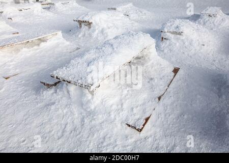 Wooden benches and desk on restaurant terrace barely visible under heavy load of snow. Concept illustrating extreme snowfall. Stock Photo