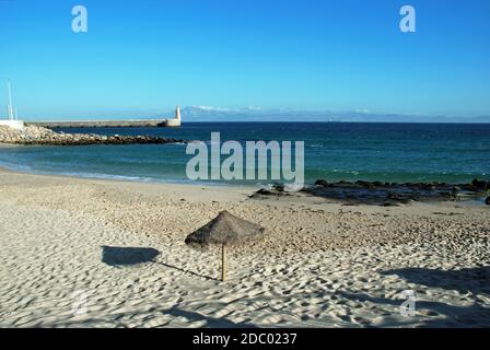 Parasol on the beach with the harbour wall entrance to the rear and views towards the Moroccan coastline and Rif mountains, Tarifa, Spain Stock Photo