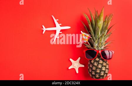 Celebrate Summer Pineapple Day Concept, Top view flat lay of funny fresh pineapple wear red sunglasses with model plane and starfish, isolated on red Stock Photo