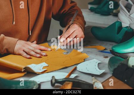 Shoemaker cutting patterns using knife from leather in his workshop. Stock Photo