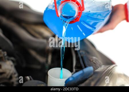 Woman pouring blue antifreeze liquid into dirty car. Stock Photo