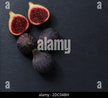 Still life of black figs. Three whole figs and one split fig. Dark Food. Stock Photo