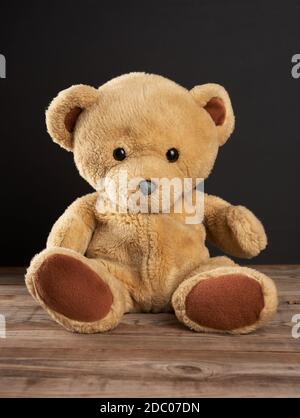 brown teddy bear sits on a wooden table, behind an empty black chalk board Stock Photo