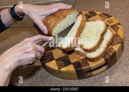 Hands slicing a white loaf of bread. Home baked. Stock Photo