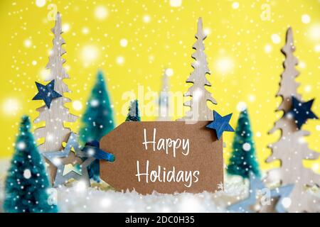 Label With English Text Happy Holidays. Christmas Trees With Star Decoration And Ornament. Yellow Background With Snow And Snowflakes Stock Photo