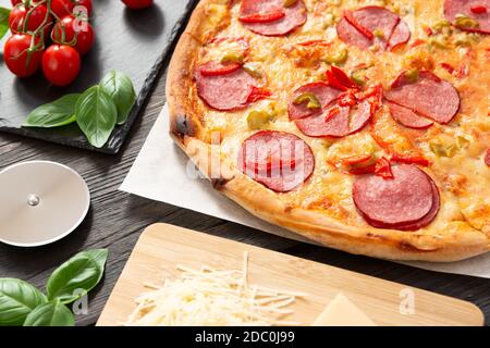 Tasty hot pizza with ingredients and pizza cutting knife on a black texture background Stock Photo