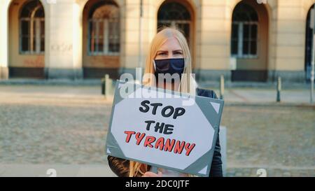 Young woman in protective mask calling to stop the tyranny by holding steamer. Protest walk in the city center. Stock Photo