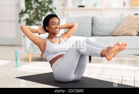 Young black woman with trained body doing abs exercise on yoga mat indoors Stock Photo