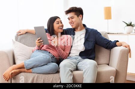 Japanese Spouses Using Tablet Browsing Internet Sitting On Couch Indoor Stock Photo