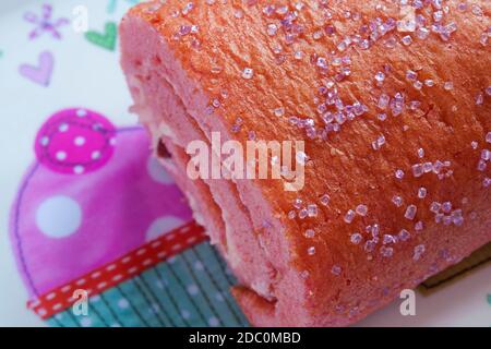 M&S Percy Pig sponge roll cake on plate - pink sponge roll filled with Percy Pig flavour buttercream and fluffy jelly pieces Stock Photo