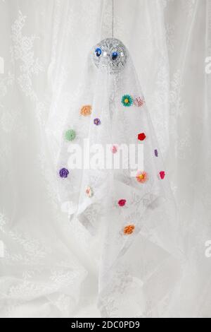 Lace curtain ghost made with a disco ball covered with multicolored flowers on the sheet. Offbeat humor and pop atmosphere. minimal color still life p Stock Photo