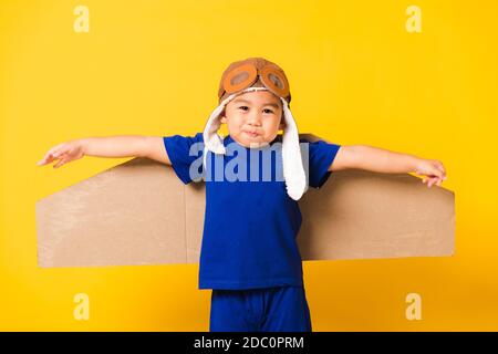 Happy Asian handsome funny child or kid little boy smile wear pilot hat playing and goggles with toy cardboard airplane wings flying, studio shot isol Stock Photo