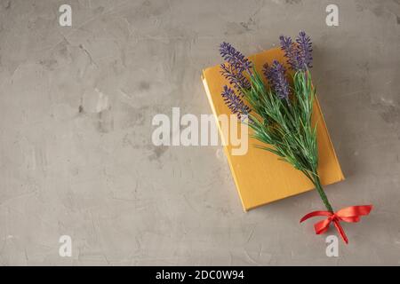 closed yellow book, lavender branch on gray cement background, top view, copy space Stock Photo