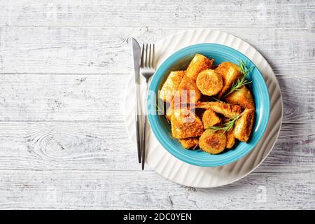 Easy side dish oven baked root vegetables: parsnip and potato wedges breaded in breadcrumbs with fresh rosemary, mustard, oregano and arugula served o Stock Photo