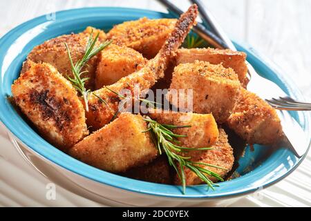 Easy side dish oven baked root vegetables: parsnip and potato wedges breaded in breadcrumbs with fresh rosemary, mustard, oregano and arugula served o Stock Photo