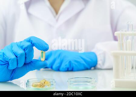 Close up Scientist hands putting in nitrile blue latex gloves holding Omega 3 capsule in labcoat wearing nitrile gloves, doing experiments in lab Stock Photo