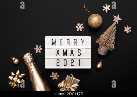 Lightbox with text MERRY XMAS 2021 and golden christmas decor on black background. Creative layout in monochrome colors Stock Photo