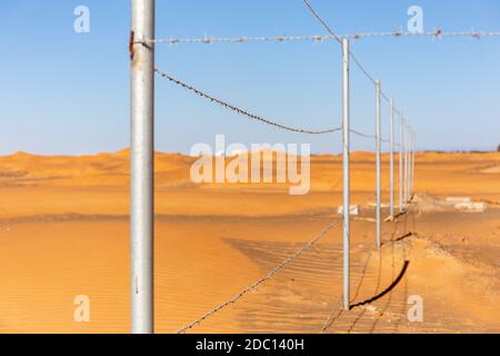 Barbed wire fence with desert dunes and blue sky in the background in Al Madam ghost village, United Arab Emirates, fence of the old mosque. Stock Photo