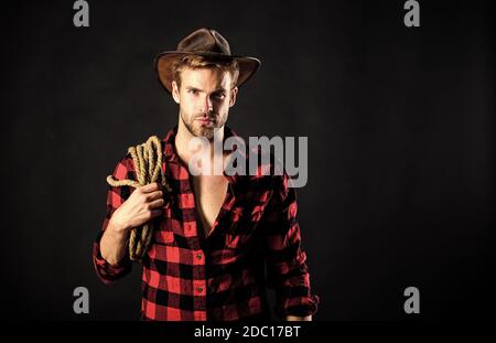 Lassoing on prairie. Lasso tool of American cowboy. Still used on ranches to capture cattle or other livestock. Western life. Man unshaven cowboy black background. Cowboy wearing hat hold rope. Stock Photo