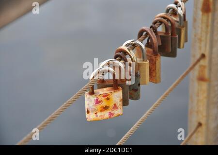 Rusty love Padlocks hanging on a iron wire on the sea water background.Many padlocks of lovers hanging on bridge railings. Stock Photo