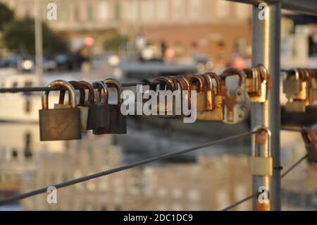 Rusty love Padlocks hanging on a iron wire on the sea water background.Many padlocks of lovers hanging on bridge railings. Stock Photo