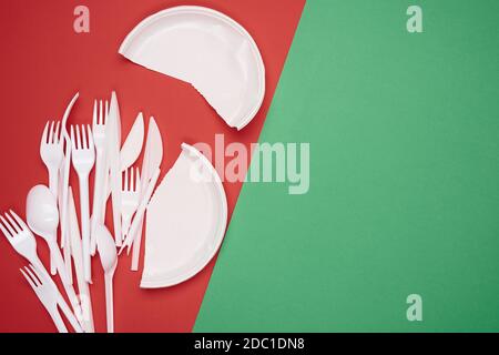 round plate and stack of plastic forks and spoons on red background, copy space Stock Photo